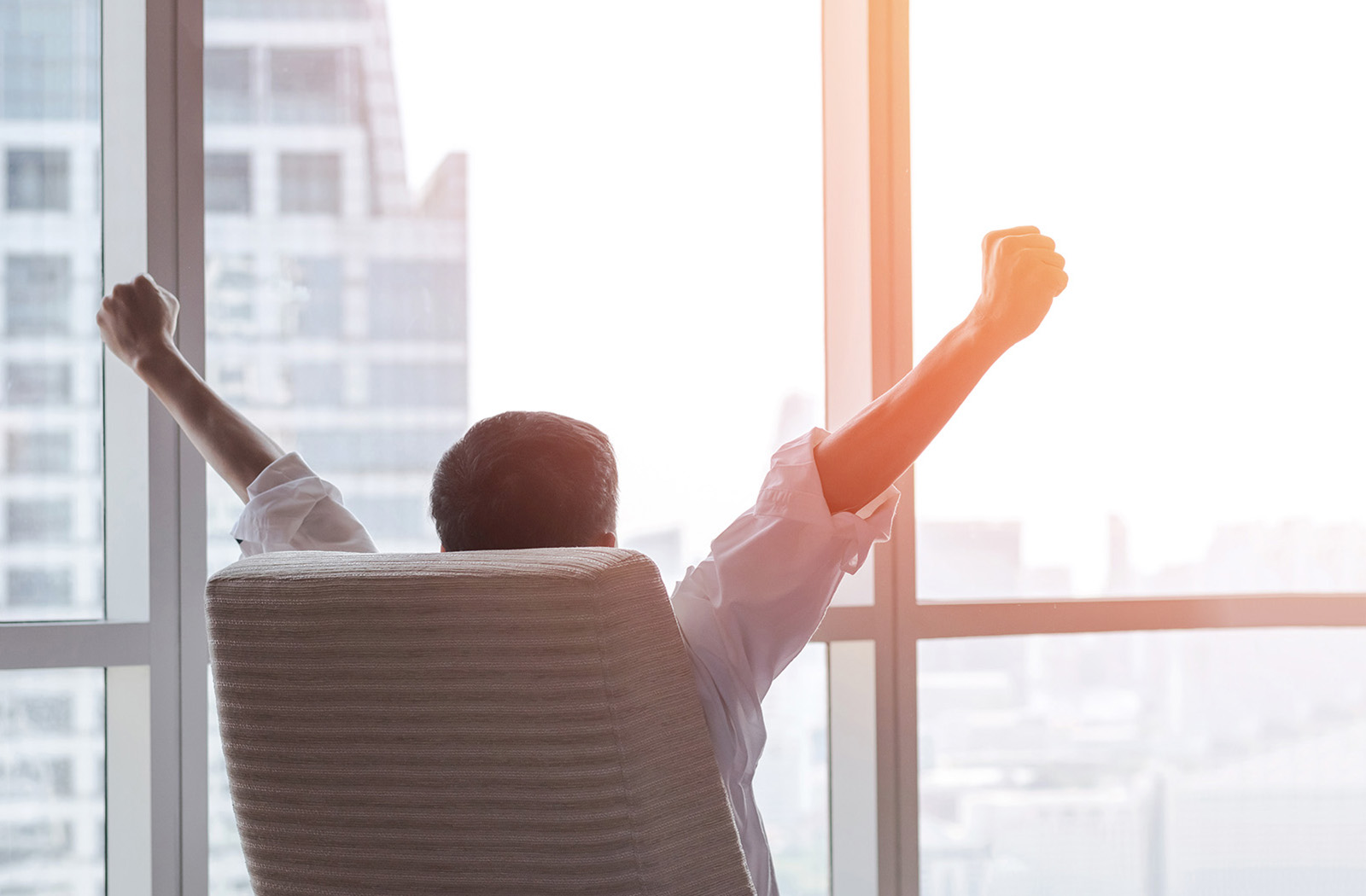 executive looking out window arms raised in victory